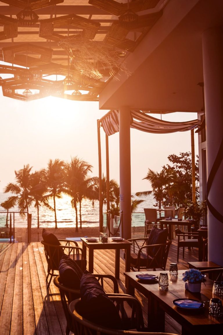 The outdoor dining area of a Florida restaurant. Tables and seats are on a wooden deck and below, on the beach.