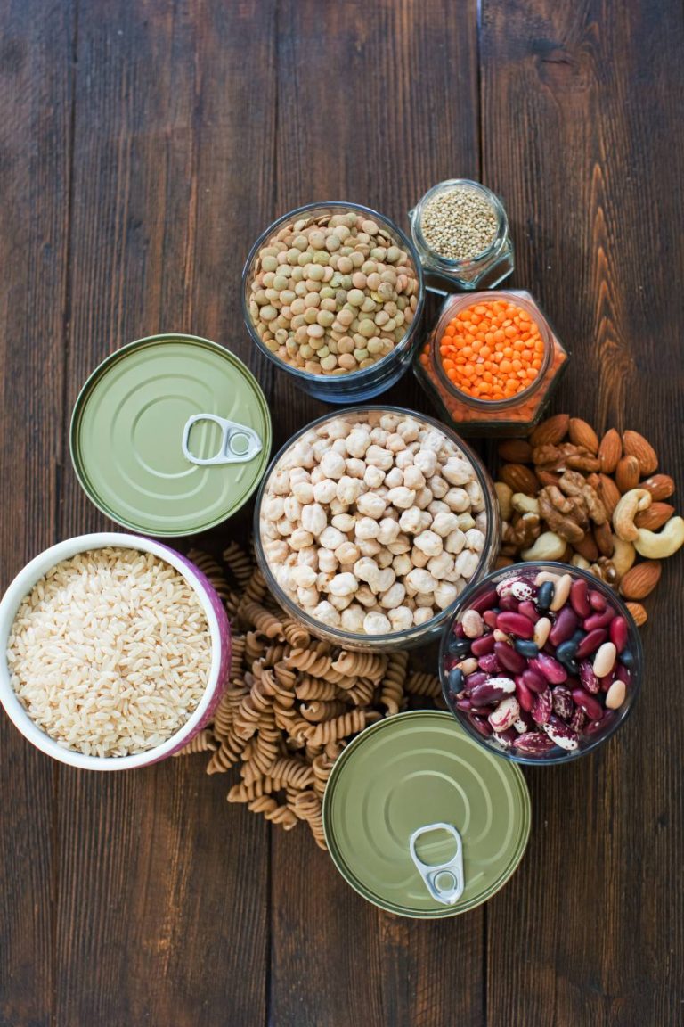 A group of non-perishable canned goods sit on a wooden table. Some of the cans are open, and some have tops on them.