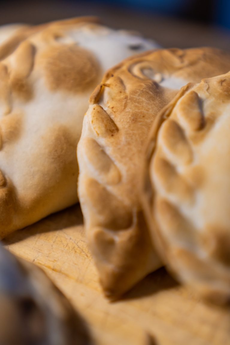 A close-up of four empanadas under dramatic lighting, served on a wooden board. The pastry looks crispy and brown.