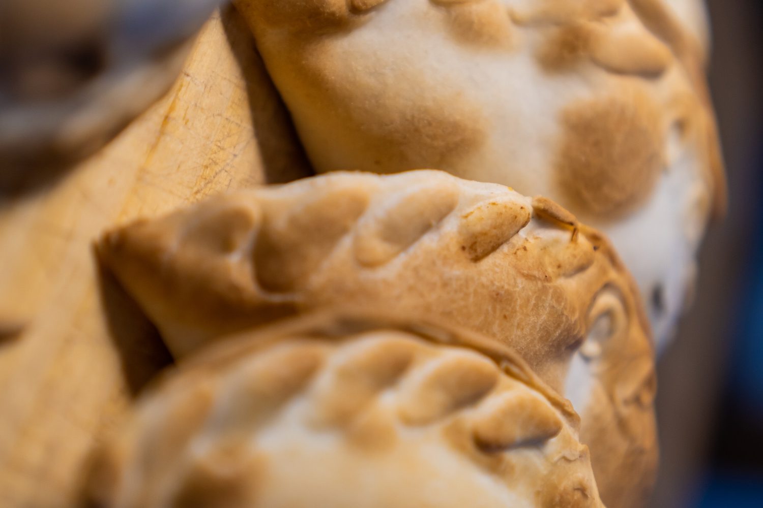 A close-up of four empanadas under dramatic lighting, served on a wooden board. The pastry looks crispy and brown.