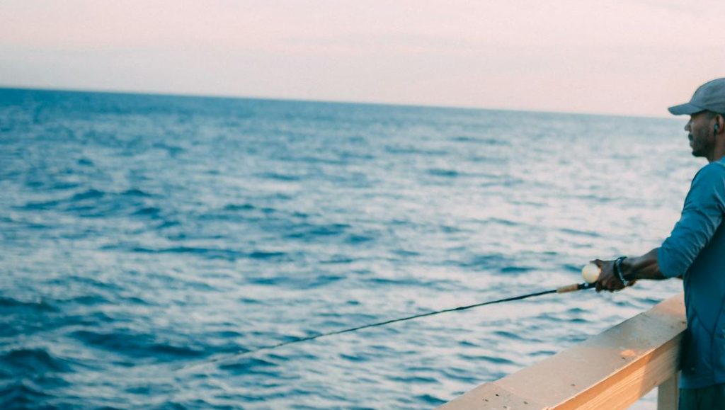 A man enjoys fishing on a sunny pier, capturing leisure and tranquility by the sea.