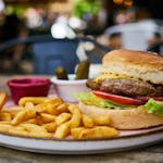Mouth-watering cheeseburger with fries, pickles, and ketchup on a wooden table outdoors.