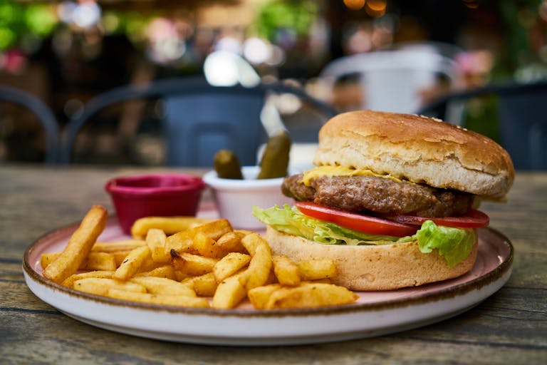 Mouth-watering cheeseburger with fries, pickles, and ketchup on a wooden table outdoors.