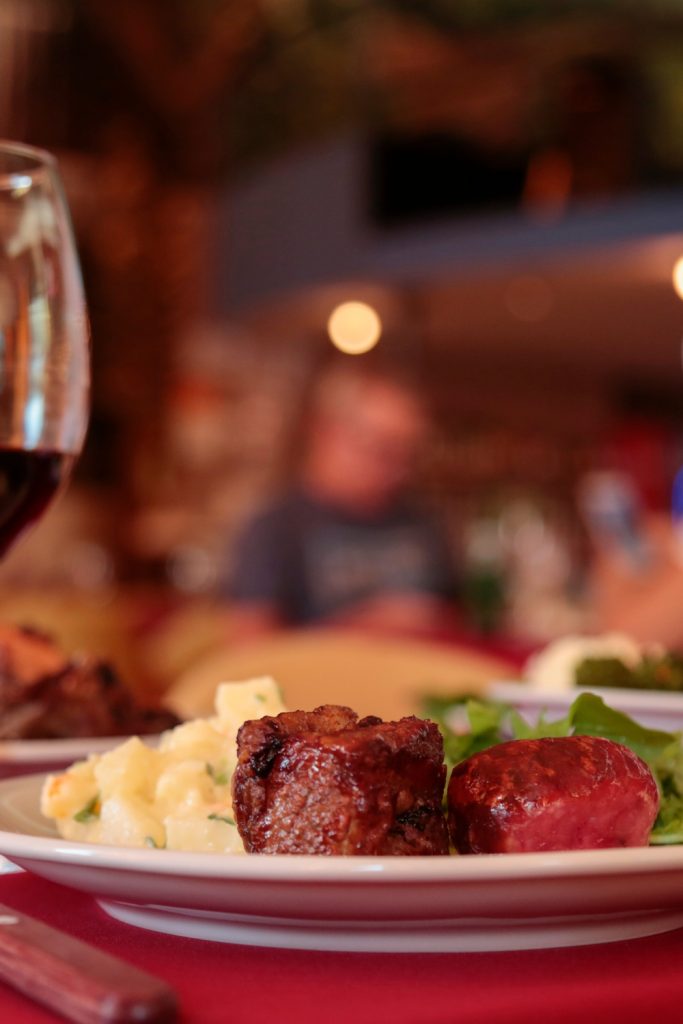 A glass of wine is on a table next to a plate filled with mashed potatoes, steak, and greens. A fork is in front of the plate.